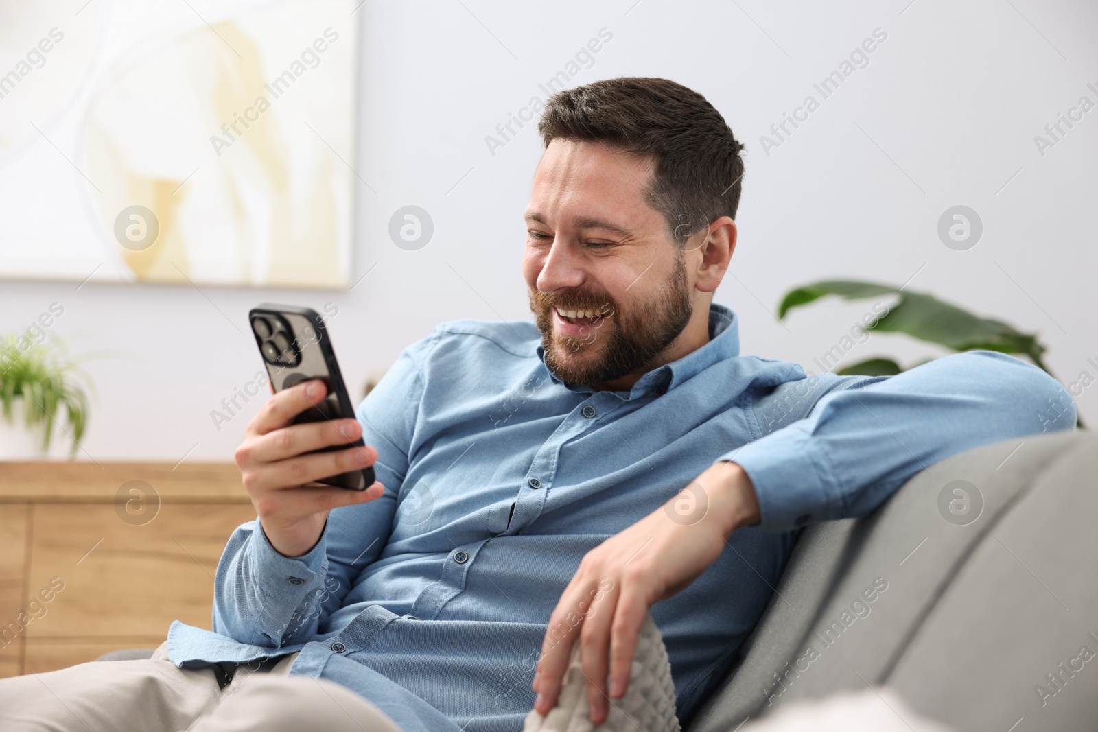 Photo of Man laughing while watching something on smartphone at home