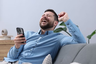 Photo of Man with smartphone laughing on sofa at home