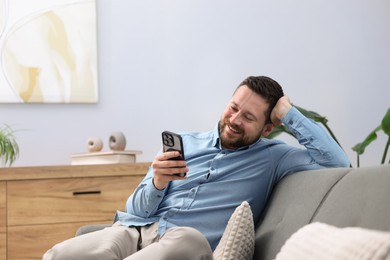 Photo of Man laughing while watching something on smartphone at home