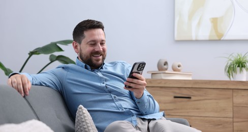 Photo of Man laughing while watching something on smartphone at home, space for text