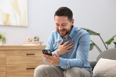 Photo of Man laughing while watching something on smartphone at home