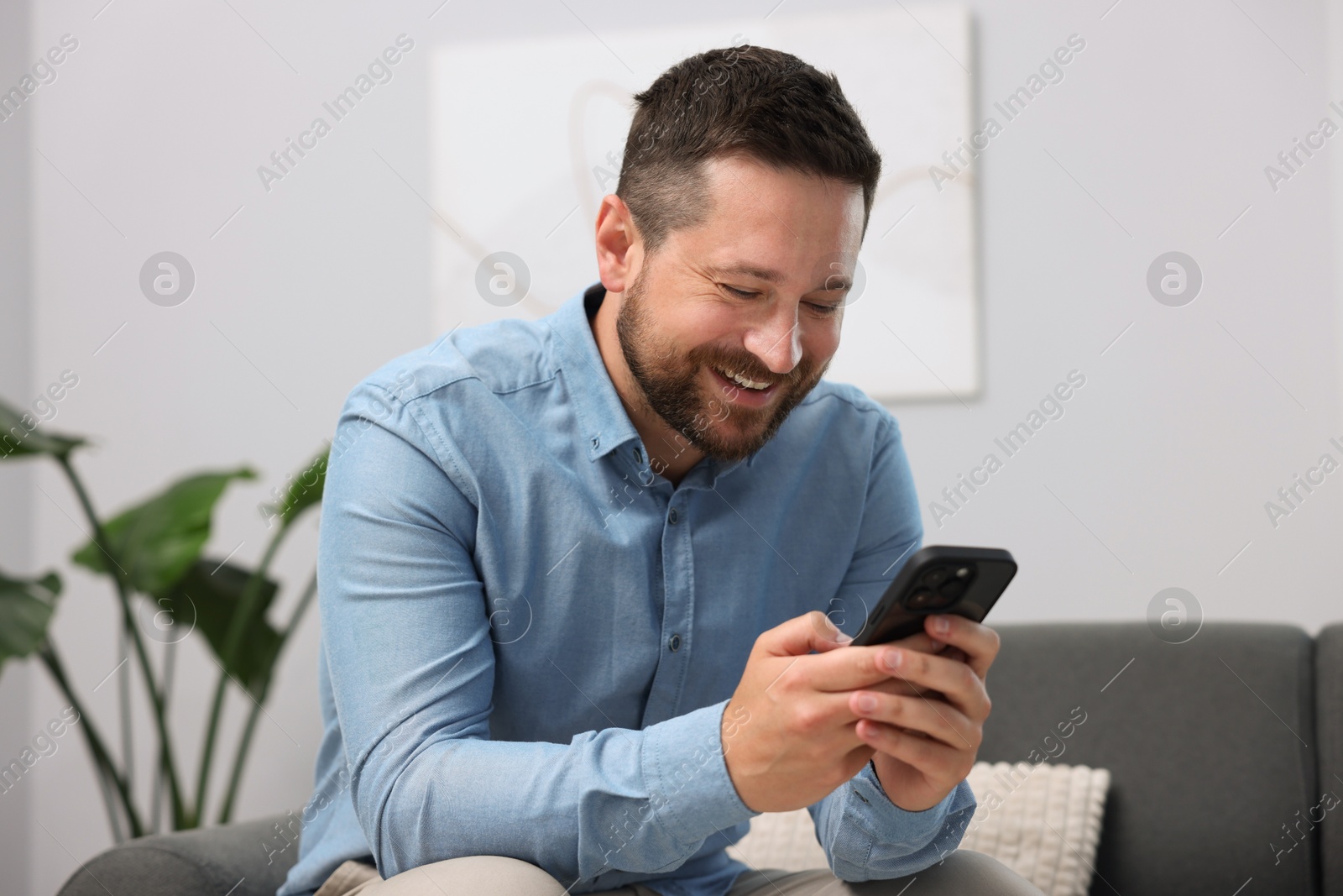 Photo of Man laughing while watching something on smartphone at home