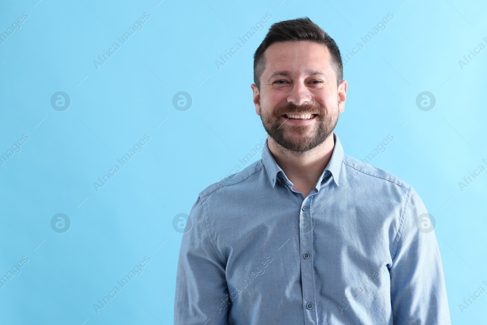 Photo of Handsome man laughing on light blue background, space for text