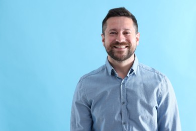 Photo of Handsome man laughing on light blue background, space for text