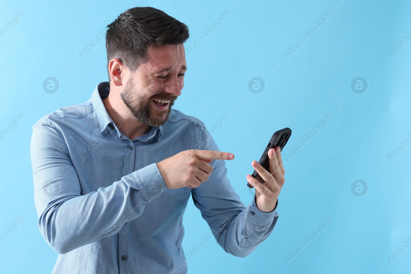 Photo of Man laughing while watching something on smartphone against light blue background, space for text