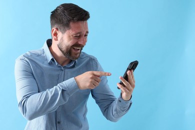 Photo of Man laughing while watching something on smartphone against light blue background, space for text