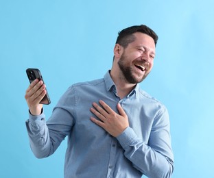 Photo of Handsome man with smartphone laughing on light blue background