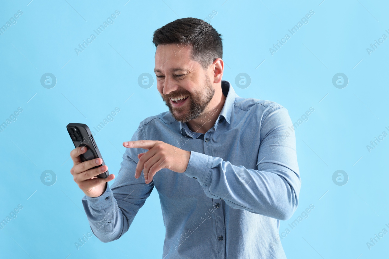 Photo of Man laughing while watching something on smartphone against light blue background