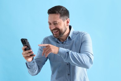 Photo of Man laughing while watching something on smartphone against light blue background