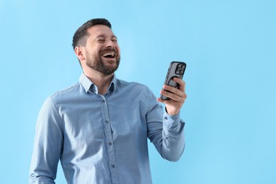 Photo of Handsome man with smartphone laughing on light blue background, space for text