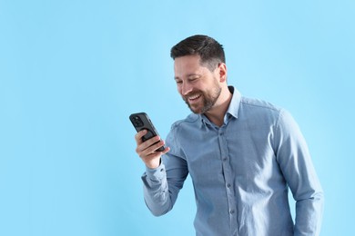 Photo of Man laughing while watching something on smartphone against light blue background, space for text