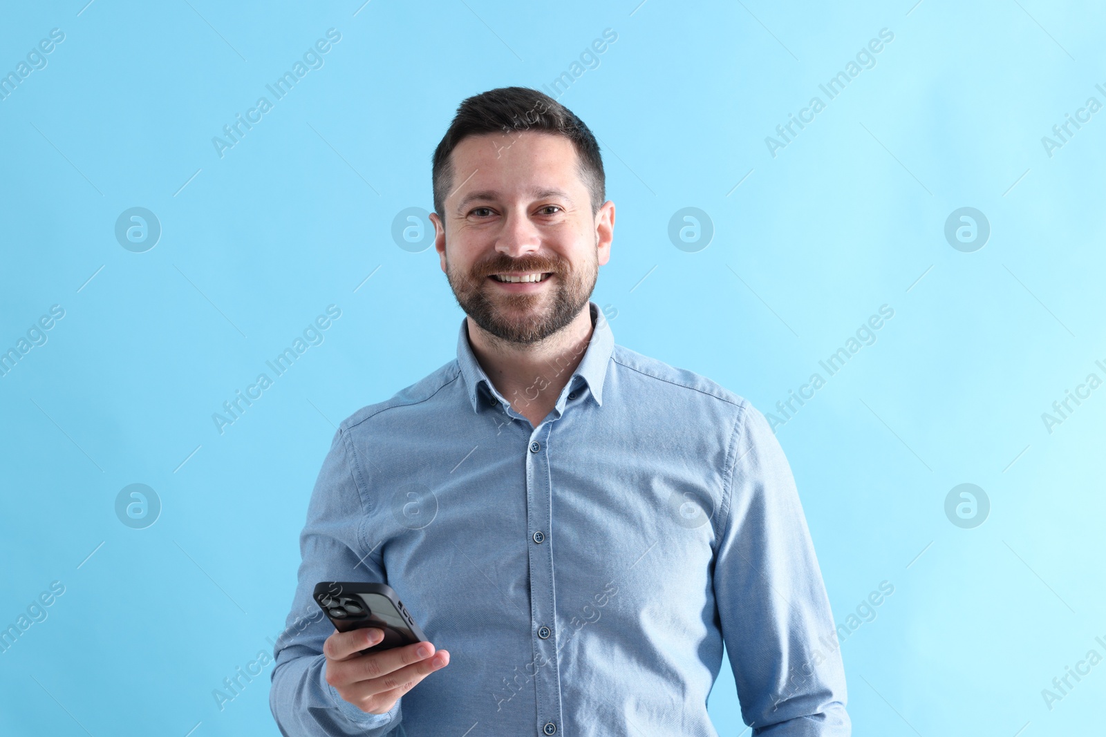 Photo of Handsome man with smartphone laughing on light blue background