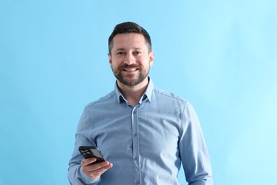 Photo of Handsome man with smartphone laughing on light blue background