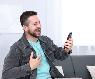 Photo of Man laughing while watching something on smartphone indoors