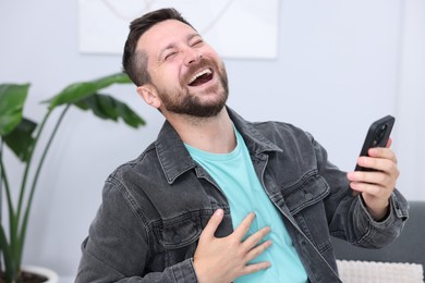 Photo of Handsome man with smartphone laughing at home