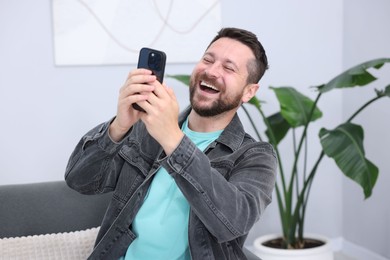 Photo of Man laughing while watching something on smartphone indoors