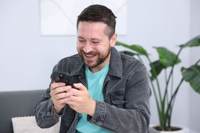 Photo of Man laughing while watching something on smartphone indoors
