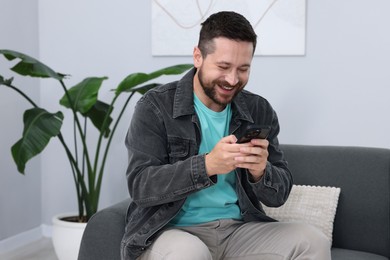 Photo of Man laughing while watching something on smartphone indoors