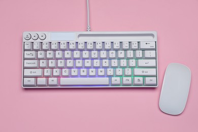 Photo of White keyboard with RGB lighting and mouse on pink background, top view