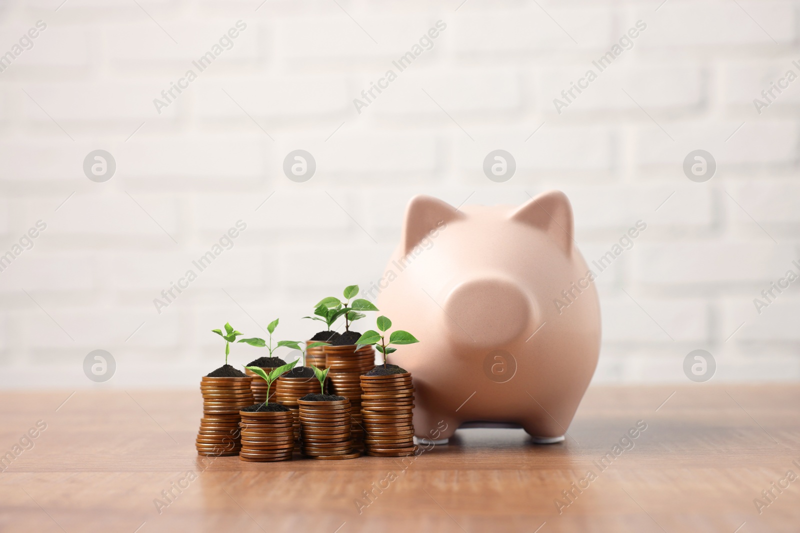 Image of Savings concept. Stacked coins with sprouts on tops and piggy bank on table
