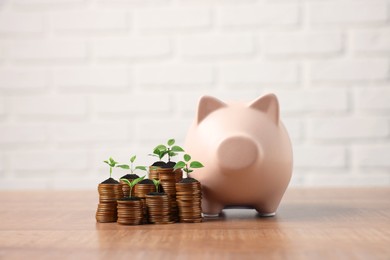 Image of Savings concept. Stacked coins with sprouts on tops and piggy bank on table