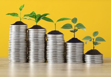 Image of Savings concept. Stacked coins with sprouts on table against orange background