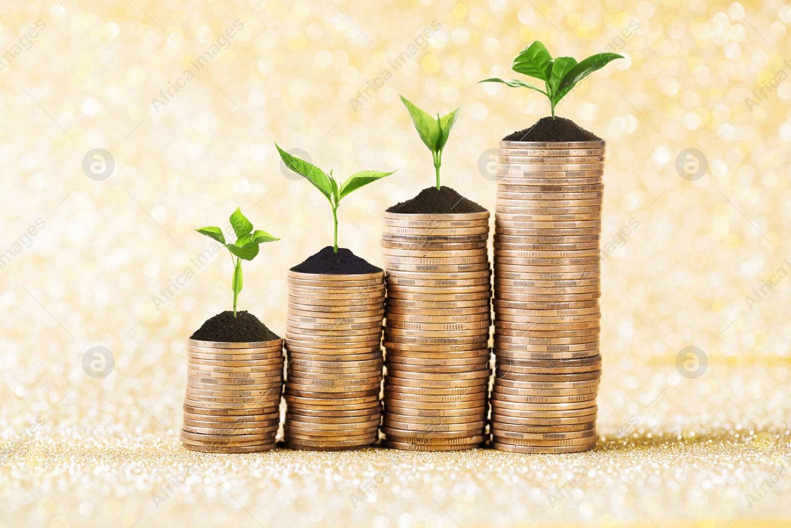 Image of Savings concept. Stacked coins with sprouts on shiny golden background