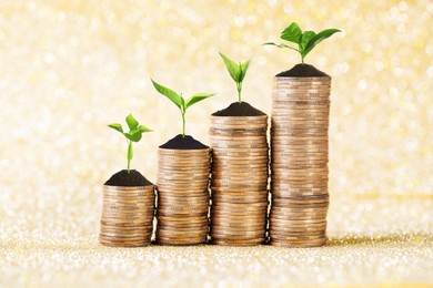 Image of Savings concept. Stacked coins with sprouts on shiny golden background