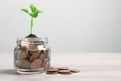 Image of Jar with coins and sprout on white table. Savings concept