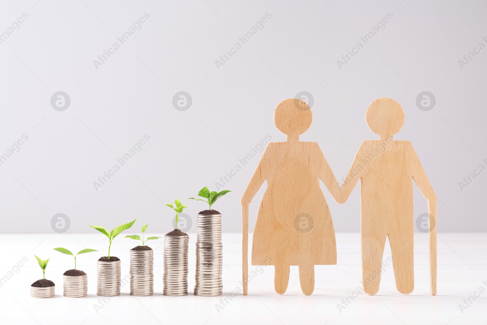 Image of Retirement savings. Stacked coins with sprouts on tops and wooden figure of two old people on table
