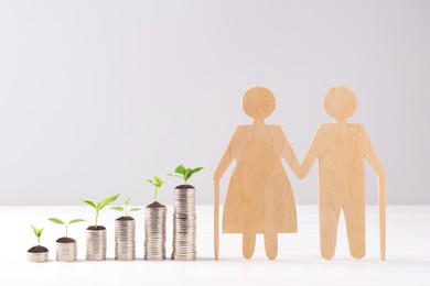 Image of Retirement savings. Stacked coins with sprouts on tops and wooden figure of two old people on table
