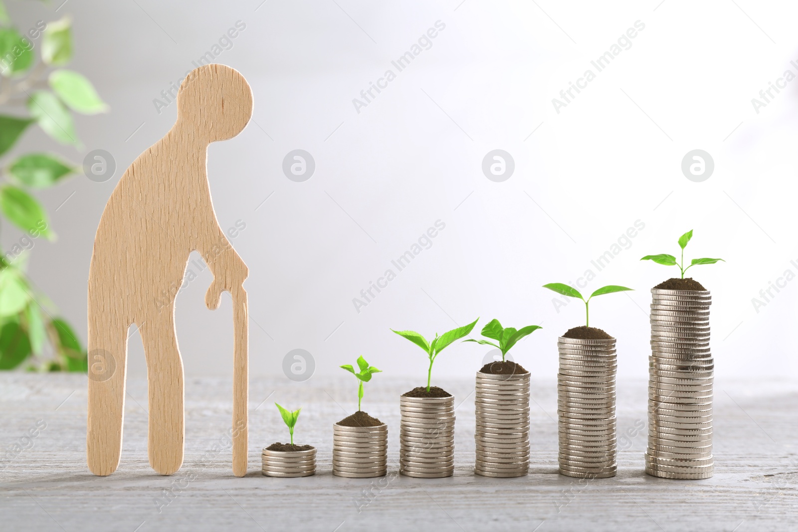 Image of Retirement savings. Stacked coins with sprouts on tops and wooden figure of old man on table