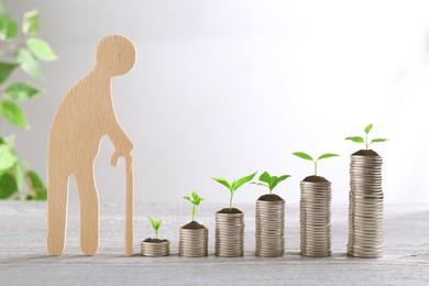 Image of Retirement savings. Stacked coins with sprouts on tops and wooden figure of old man on table