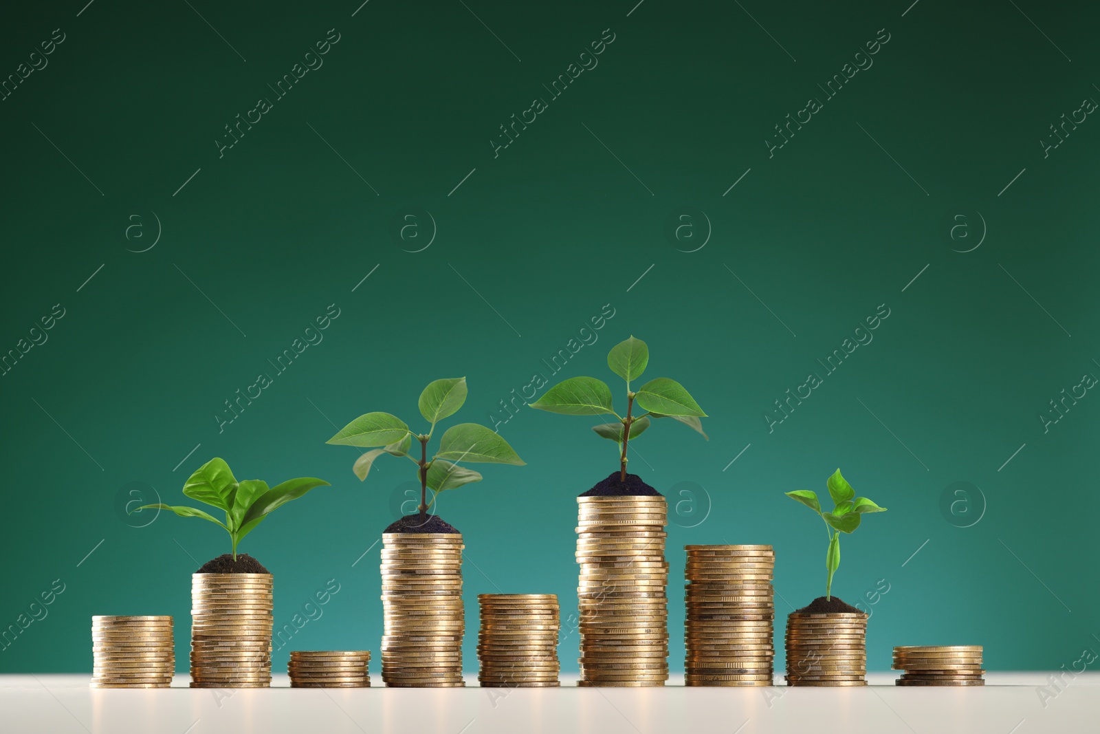 Image of Savings concept. Stacked coins with sprouts on table against green background