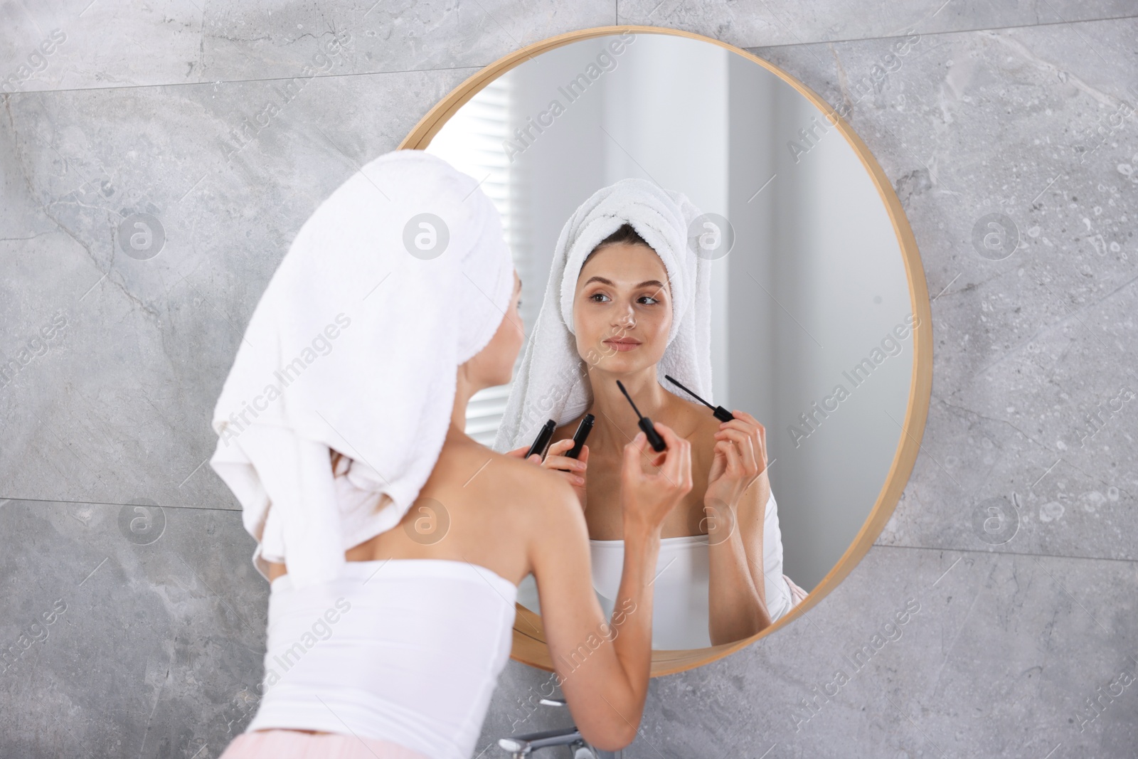 Photo of Getting ready. Young woman applying mascara near mirror at home