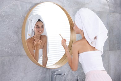 Photo of Getting ready. Young woman brushing her teeth near mirror at home