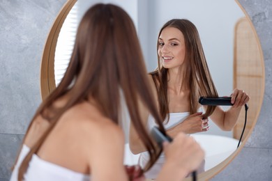 Photo of Getting ready. Young woman using hair straightener at home