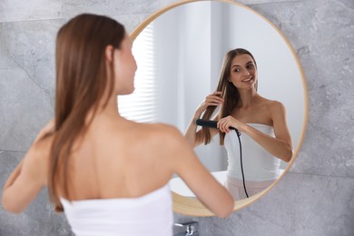 Photo of Getting ready. Young woman using hair straightener at home