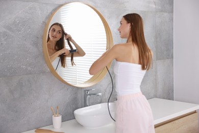 Photo of Getting ready. Young woman using hair straightener at home