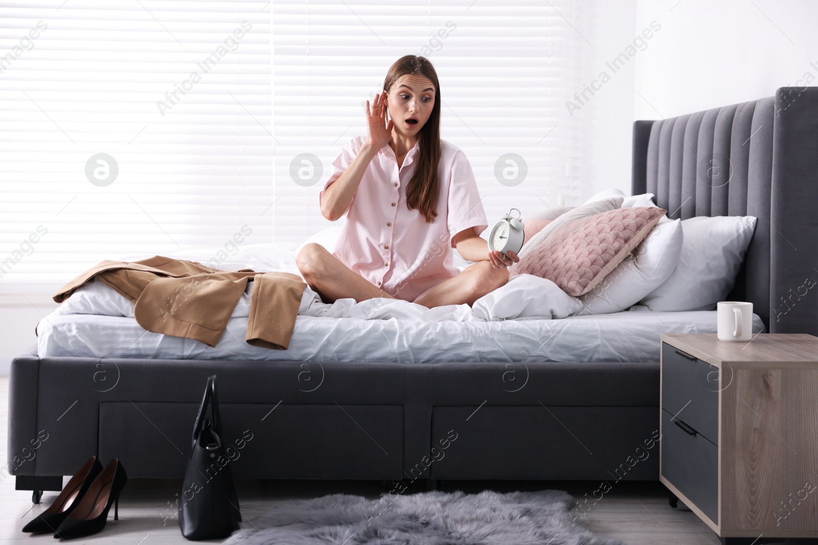 Photo of Getting ready. Surprised young woman looking at alarm clock indoors