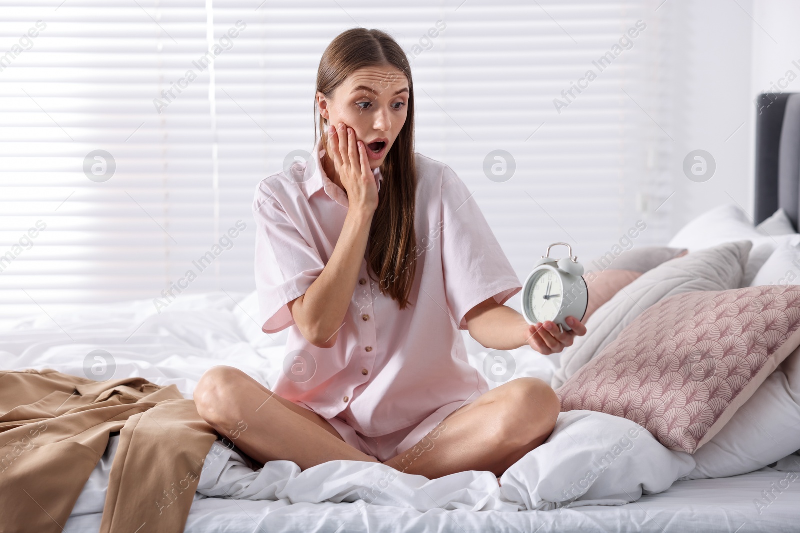 Photo of Getting ready. Surprised young woman looking at alarm clock indoors