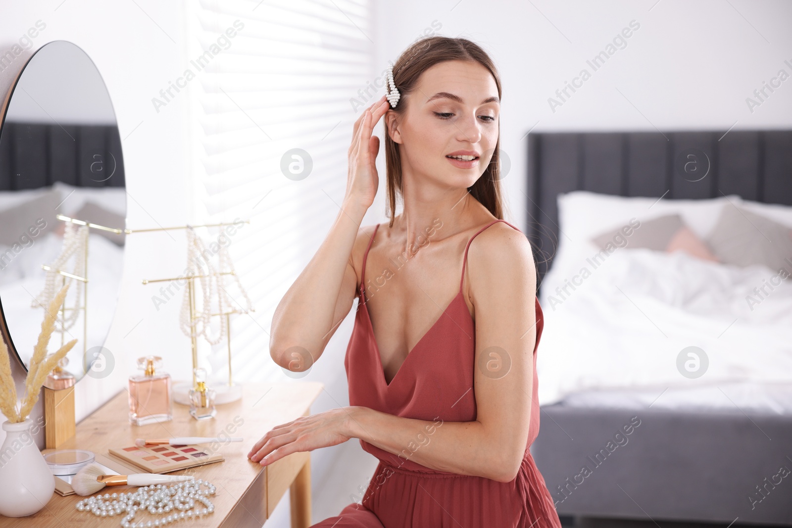Photo of Getting ready. Young woman with stylish hair clip near mirror at vanity indoors
