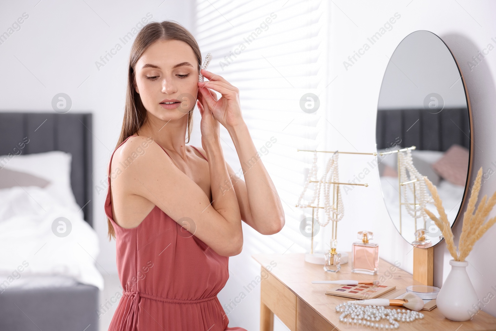 Photo of Getting ready. Young woman with stylish hair clip near mirror at vanity indoors
