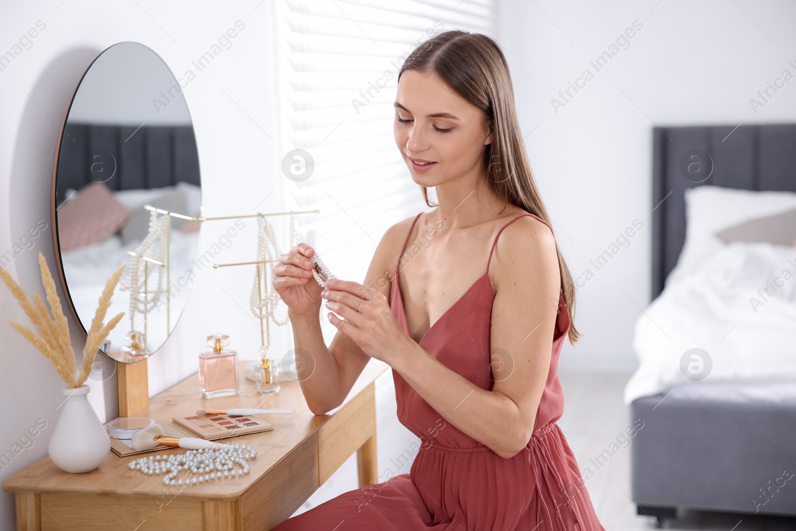 Photo of Getting ready. Young woman with stylish hair clip near mirror at vanity indoors