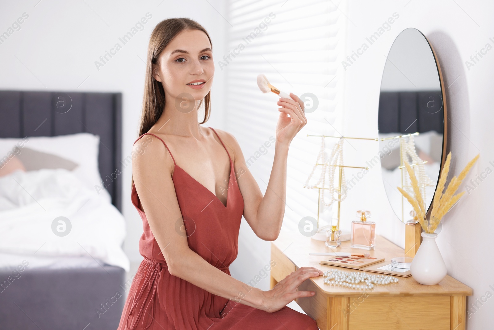 Photo of Getting ready. Young woman applying makeup near mirror at vanity indoors