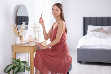 Photo of Getting ready. Young woman applying makeup near mirror at vanity indoors