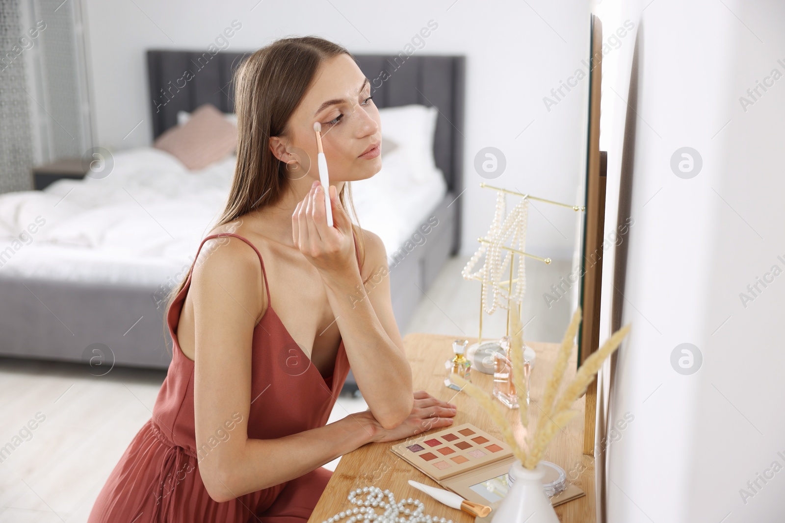 Photo of Getting ready. Young woman applying makeup near mirror at vanity indoors
