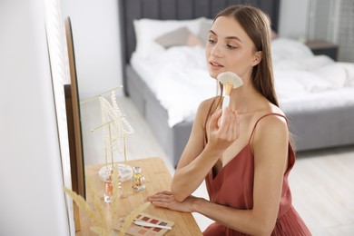 Photo of Getting ready. Young woman applying makeup near mirror at vanity indoors