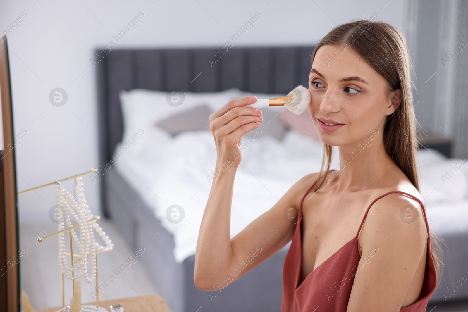 Photo of Getting ready. Young woman applying makeup near mirror at vanity indoors