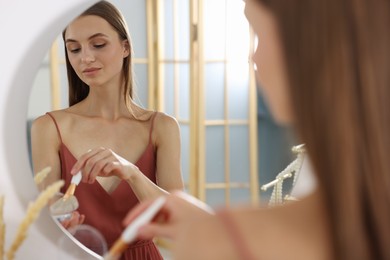 Photo of Getting ready. Young woman applying makeup near mirror at vanity indoors